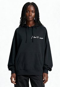 Sweatshirt à capuche noir avec poche avant, comportant un texte blanc en cursive "I don't care" sur la poitrine. Tissu doux, coupe décontractée, et poignets côtelés.