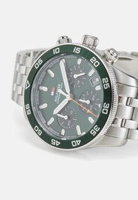 Montre-bracelet chronographe avec un bracelet en acier inoxydable, un cadran vert, des marqueurs argentés et une lunette. Elle dispose de trois sous-cadrans et d'une trotteuse orange.