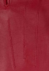 Czerwona skórzana rękawica o gładkiej teksturze, z trzema pionowymi przeszyciami z tyłu dla dodatkowego efektu wizualnego.