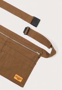 Pruunist kehast valmistatud vöökott, millel on lukuga tasku, reguleeritav rihm ja oranž silt. Omab metallnuppe ja sujuvat tekstuuri.