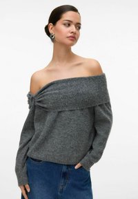 Grauer schulterfreier Strickpullover mit weicher Textur, langen Ärmeln und einer Knotenverzierung an der Schulter, kombiniert mit einem blauen Jeansrock.