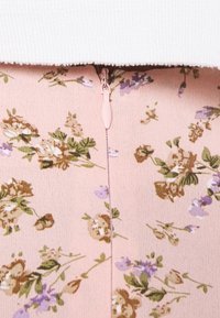 Tela con un patrón floral en suave rosa, con flores en verde, marrón y púrpura. Presenta una cremallera rosa clara en el centro.