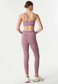 Lavendel sportbeha met een geknoopte band, gecombineerd met bijpassende hoog ingezette leggings. Beide stukken zijn gemaakt van een gladde, rekbare stof.