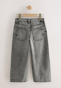 Grijze denim wijde broekspijpen, hangend aan een houten hanger, met twee achterzakken en gestikte details. Strakke afwerking aan de zoom.