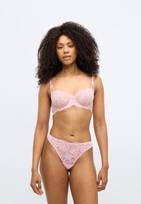 Ensemble soutien-gorge en dentelle rose et string avec motifs floraux, bords festonnés et fines bretelles. Le tissu semble délicat avec une texture douce.