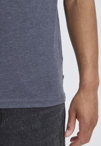 Gray short-sleeve shirt made of soft fabric, featuring a straight hem and a small tag on the side. Hand positioned near the shirt.