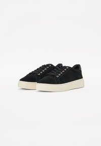 Sneakers neri in suede con suole in gomma crema. Presentano occhielli dorati e una finitura testurizzata. Design classico con lacci e branding minimale.