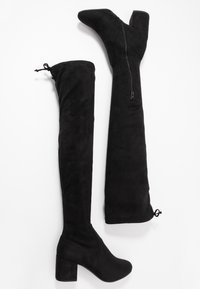 Botas negras hasta el muslo hechas de un material suave similar al ante. Cuentan con un tacón ancho, punta afilada y cremallera lateral para el cierre. Tienen un cordón en la parte superior.
