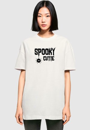 Creme oversized t-shirt lavet af bomuld, med en sort grafik der står "SPOOKY CUTIE" med en edderkop, korte ærmer og rund halsudskæring.
