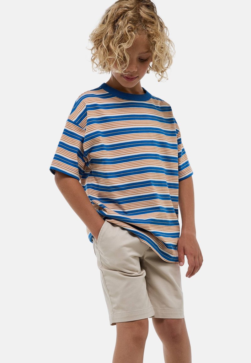 T-shirt rayé bleu, orange et beige avec des manches courtes et un col bleu. Associé à un short beige. Tissu doux, coupe décontractée.