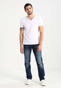 Witte katoenen V-hals t-shirt gecombineerd met blauwe denim jeans. De jeans hebben een vervaagde wasbeurt en frontzakken. Witte sneakers maken de outfit compleet.