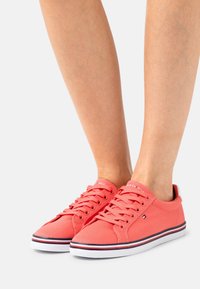 Korallfärgade kanvas sneakers med vita gummisulor. Har snörning, logotyp på tungan och subtila sidostygn med röda och blå detaljer.