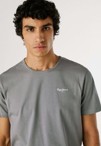 T-shirt grigio a maniche corte con scollo rotondo e piccolo logo bianco sul lato sinistro del petto. Tessuto morbido con dettagli di trame minime.