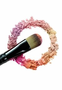 Makeupborste med ett brett, runt, mjukt borsthuvud, på en cirkulär anordning av färgat puder som reflekterar nyanser av rosa, orange och beige.