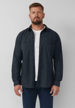 Dunkelblaues Langarmhemd mit Knopfleiste, zwei Brusttaschen, Kragen und umgeschlagenen Ärmeln, getragen über einem weißen T-Shirt. Glatte Textur.