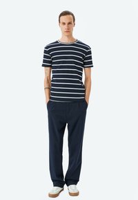 Navy-gestreiftes T-Shirt mit weißen horizontalen Linien, kombiniert mit navyblauen, gefalteten Hosen und weißen Sneakers mit braunen Sohlen.