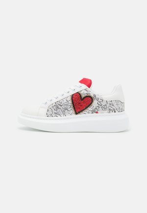 Baskets blanches avec un design argenté texturé, comprenant une grande application en forme de cœur rouge, un accent rouge sur la zone des lacets et une semelle épaisse blanche.