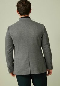 Grau maßgeschneiderte Blazer mit dezentem Fischgrätenmuster, Reverskragen, zwei Knöpfen und einer mittigen Lüftungsöffnung, gefertigt aus strukturiertem Stoff.