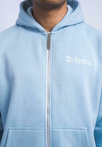 Light blue zip-up hoodie made from soft fabric. Features a front zipper, two pockets, and "Dropsize" embroidered in white.