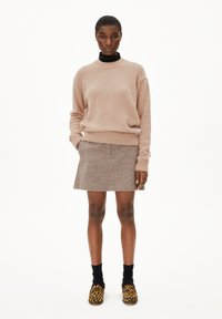 Lichtroze gebreide trui met geribbelde boorden, gecombineerd met een bruine rok en zwarte sokken. Schoenen met een luipaardprint design.