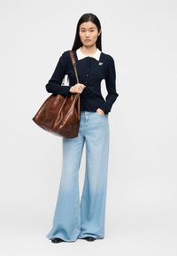 Μπλε ναυτικό ριμπ ζακέτα με κουμπιά, ανοιχτό μπλε τζιν με καμπάνα και μεγάλη καφέ δερμάτινη τσάντα με λουράκι ώμου. Γιακάς σε αντίθετο χρώμα.