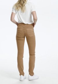 Bruna slim-fit jeans med bakfickor och sömnadsdetaljer, i kombination med en kortärmad vit skjorta och vita sneakers, sedd bakifrån.