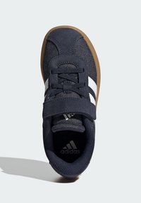 Námořnické modré tenisky s svrškem z nubukové kůže a tkaniny, polstrovaným límcem, bílými pruhy a gumovou podrážkou; obsahují šňůrky a pásku.