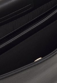 Svart läderhandväska inuti med en slät yta, fodrad fack med dragkedja och en ytterligare ficka med subtila gulddetaljer.