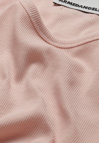 Lichtroze geribde top met een ronde halslijn. Zachte textuurstof met zichtbaar ribbelpatroon. Merketiket "ARMEDANGELS" bij de kraag.