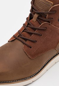 Bruine leren laars met een bovenwerk van suede, contrasterende veters, een ronde neus en een roomkleurige zool met zichtbare stikdetails.