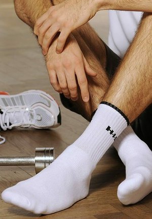 White athletic socks with black ribbed cuff, featuring a logo on the front. Close-up shot with a dumbbell and sneakers in background.