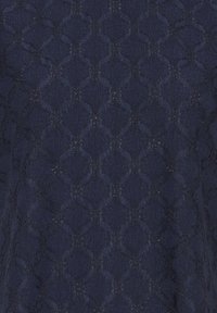 Tissu bleu marine avec un motif en dentelle en forme de losange présentant des détails texturés et ajourés.