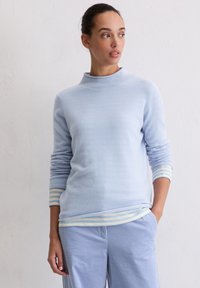 Hellblauer Pullover mit hohem Kragen und langen Ärmeln, verziert mit gestreiften Akzenten in sanften Farbtönen an den Bündchen. Kombiniert mit einer passenden blauen Hose.