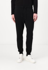 Black jogger pants made of soft fabric, featuring an elastic waistband with drawstrings, cuffed ankles, and a slim fit design.