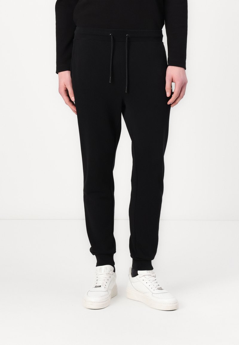 Black jogger pants made of soft fabric, featuring an elastic waistband with drawstrings, cuffed ankles, and a slim fit design.