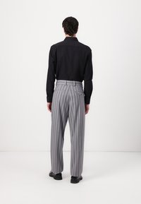 Black collared shirt, gray pinstriped trousers with pleats and side pockets, polished shoes, viewed from the back against a white background.