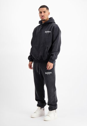 Zwart hoodie- en broekset, met een voorzak, logo-print en een zachte textuur. Gecombineerd met witte sneakers.