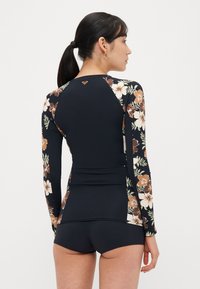 Lange mouwen zwemtop met een bloemenpatroon in aardetinten op een donkere achtergrond. Heeft een aansluitend ontwerp en shorts met een hoge taille.