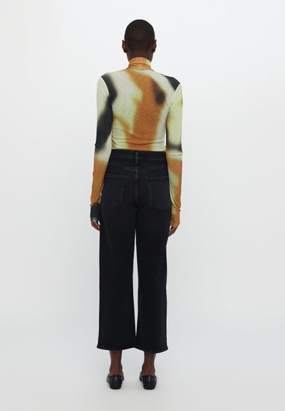 Long-sleeve, fitted top with an abstract orange, black, and green pattern; paired with high-waisted, wide-leg black denim jeans.