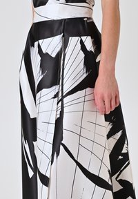 Jupe noire et blanche avec un motif de coups de pinceau abstrait, en satin, taille haute, fente sur le côté et détails de boutons décoratifs.