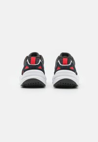 Svart- och grå sneakers med vit sula, röda detaljer, texturerat tyg och utskurna detaljer nära hälen för ventilation.