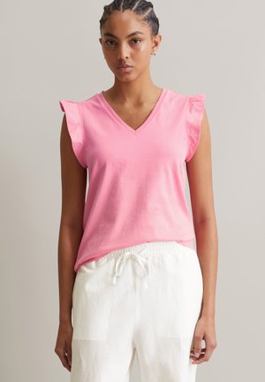 Pink cotton top with a V-neckline and ruffled sleeves, paired with white drawstring pants. Smooth texture and casual fit.