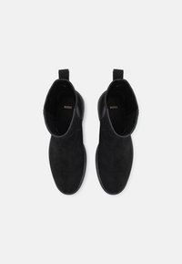 Bottes chevilles en daim noir à texture lisse, dotées de languettes de tirage et d'un bout arrondi. Design minimaliste avec un marquage discret sur la semelle intérieure.