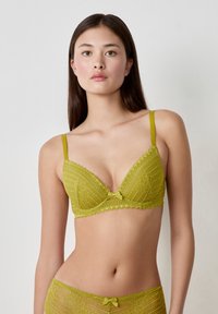 Bra verde oliva con pizzo, scollato e con spalline regolabili. Presenta motivi floreali intricati e un fiocco al centro.