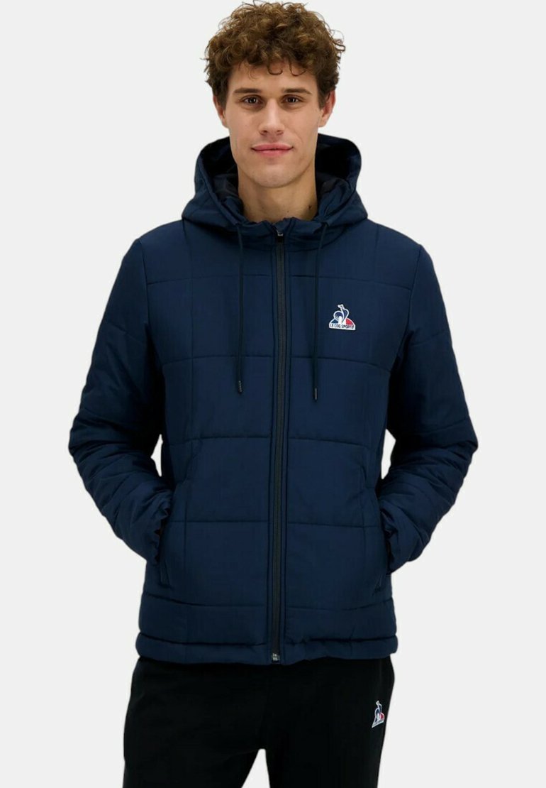 Giacca imbottita navy con cappuccio regolabile, cerniera frontale e tasche laterali. Presenta un piccolo logo sul petto. Texture liscia.