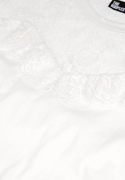 Hvid bomulds t-shirt med en blondeflæse ved halsudskæringen, med en glat tekstur og diskret glans. Brandmærket er synligt.