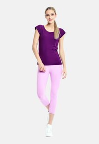 Purple short-sleeve top paired with light pink capri leggings. Loose fit, smooth texture, worn with white athletic shoes.