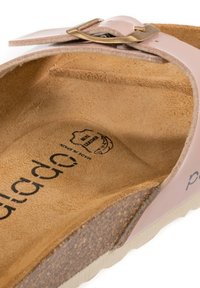 Ljust rosa sandal med bred rem, guldfärgad spänne och formad fotbädd i kork. Har en strukturerad undersida och tryck av logotyp.