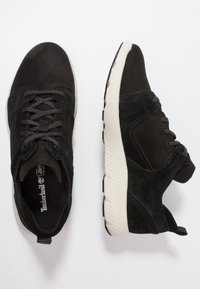 Svarta mocka- och textilsneakers med snörningsdesign, kontrasterande vit mellansula och texturerad gummisula. Har en dragflik på hälen.