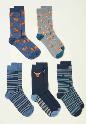 Piecas vīriešu zeķu pāri ar dažādiem rakstiem: Īru govju attēli, svītras un viendabīgas krāsas zilā, pelēkā un tirkīza toņos, ar kontrastējošām purngala detaļām.